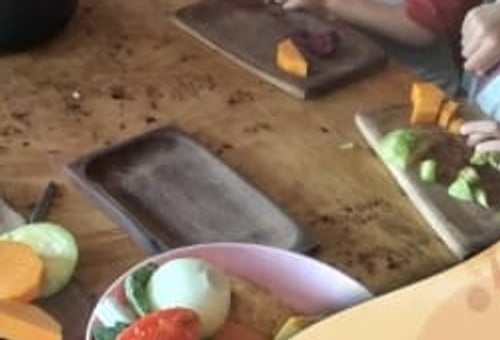 Manos de niños cortando verduras sobre tablas de madera